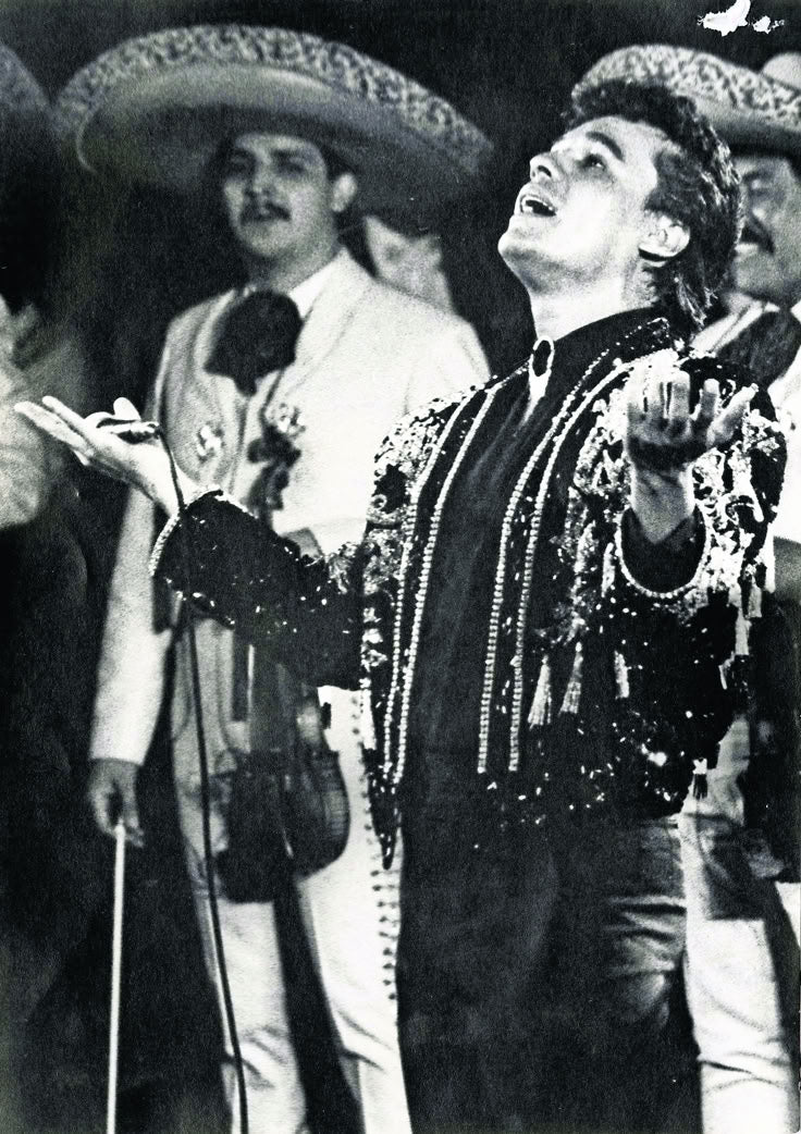 Juan Gabriel performing in a decorated charro jacket with mariachis behind him